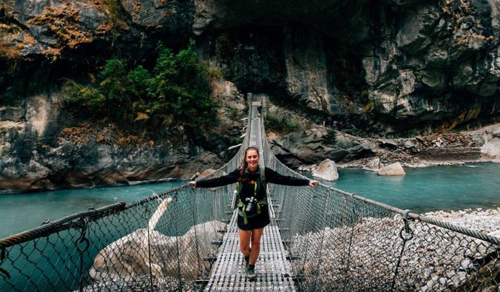 Trekker crossing a suspension bridge on a wet post-monsoon trail in Nepal during early autumn trekking season